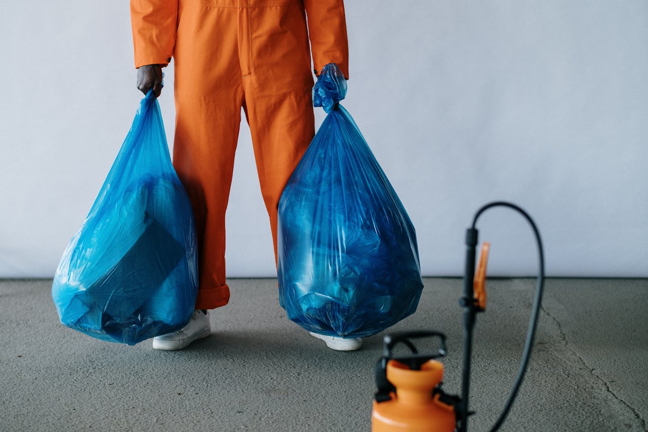 Services Sanitation worker in orange overalls holding blue trash bags indoors for waste management.